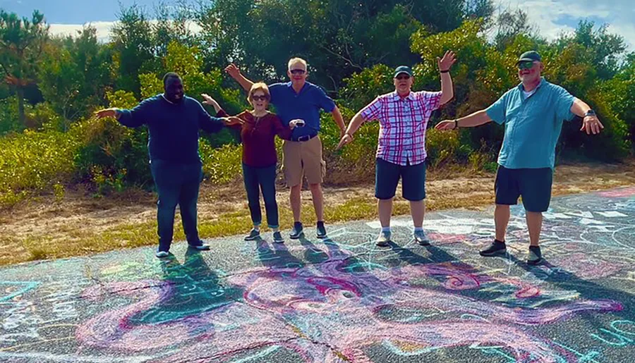 A group of people is standing with raised arms on a colorful chalk-drawn pattern on the ground, appearing cheerful and playful under a bright sky.