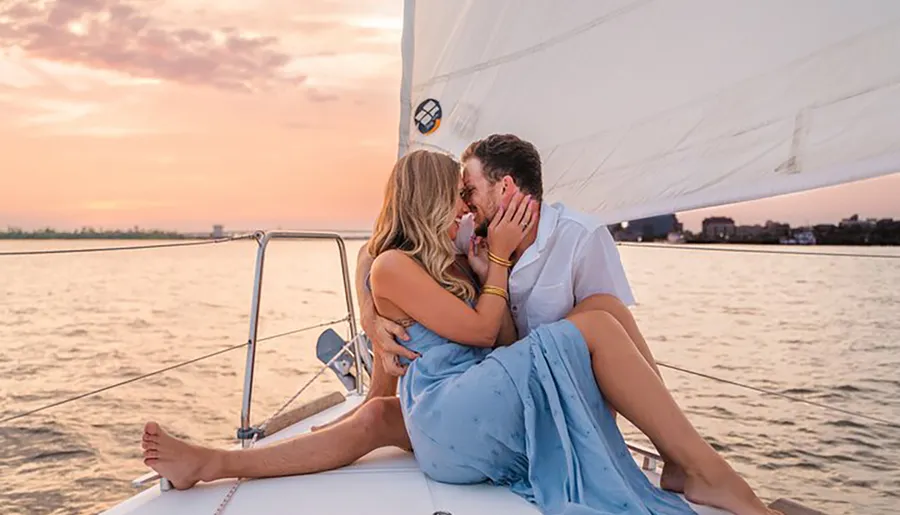 A couple shares an intimate moment on the bow of a sailboat at sunset.