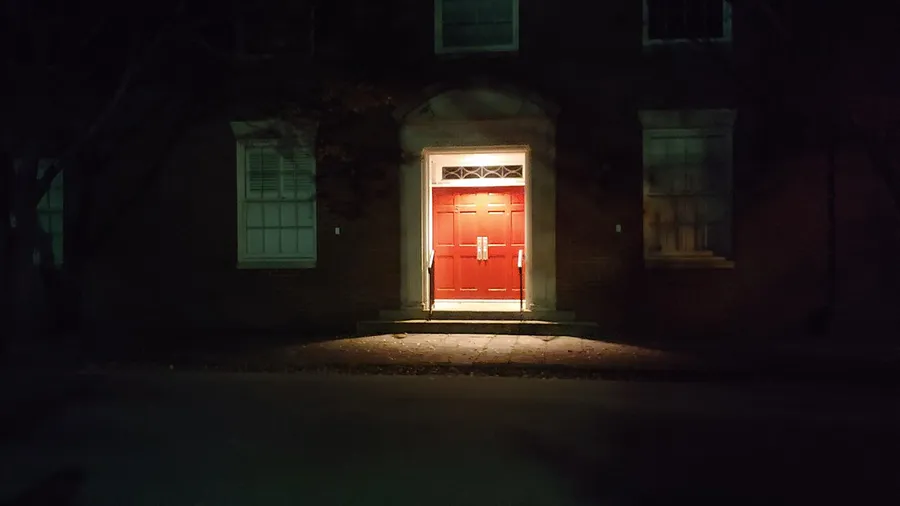 A red door of a building is illuminated by an overhead light at night.