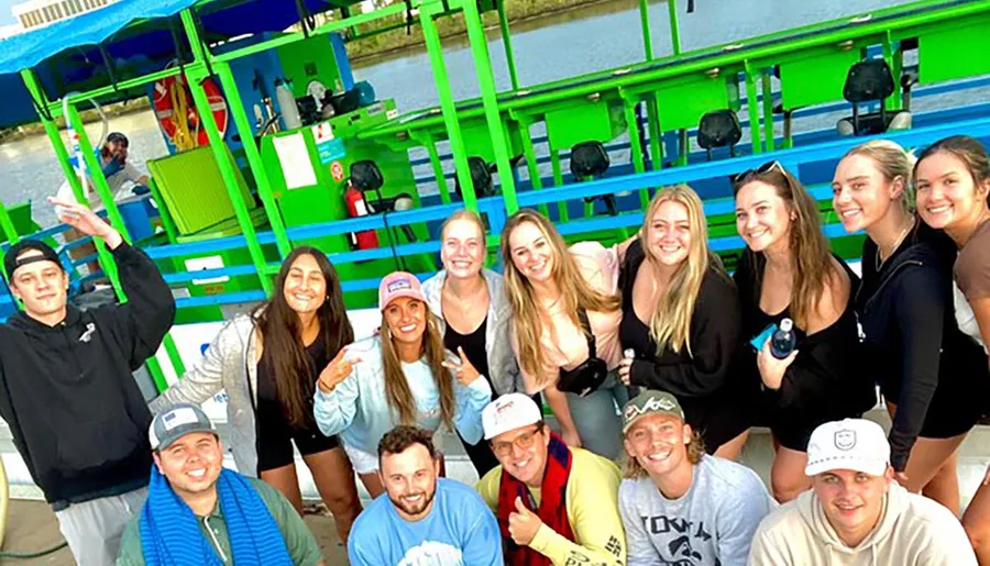 A group of smiling young adults is posing for a photo in front of a colorful pedal boat structure on a dock.