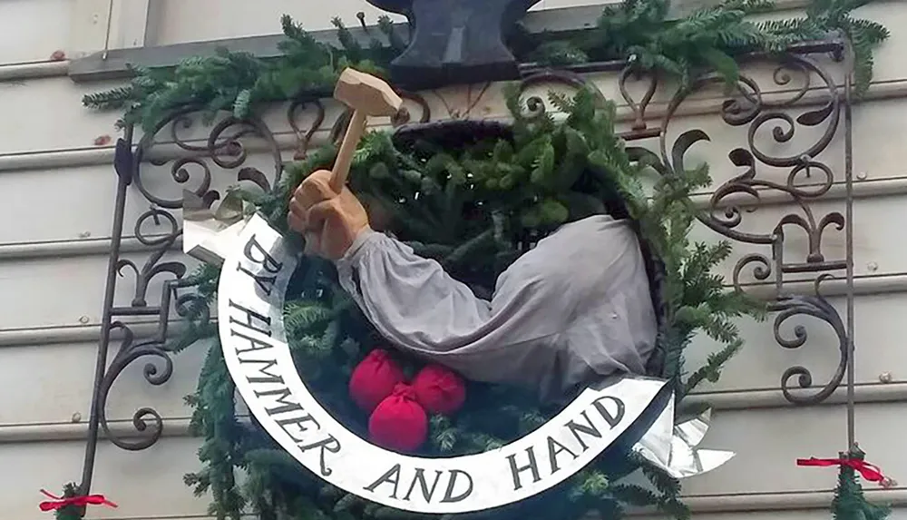 The image shows a festive wreath hung on a wall incorporating a three-dimensional figure of an arm holding a hammer adorned with a banner that reads HAMMER AND HAND