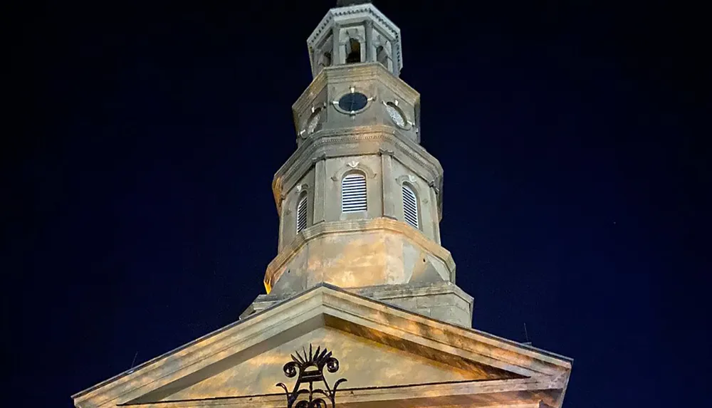 The image captures the illuminated steeple of a historic building against the night sky showcasing architectural details and a weathervane