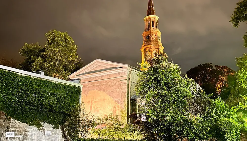 The image captures a night scene of a well-lit church tower rising above surrounding trees under a dark ominous sky