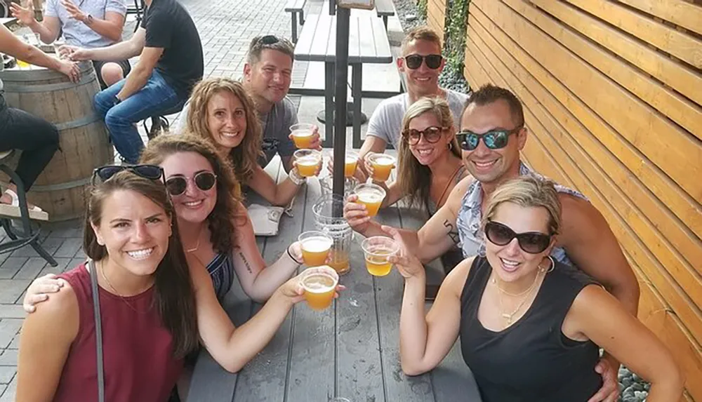 A group of smiling friends are enjoying drinks and posing for a photo at an outdoor bar