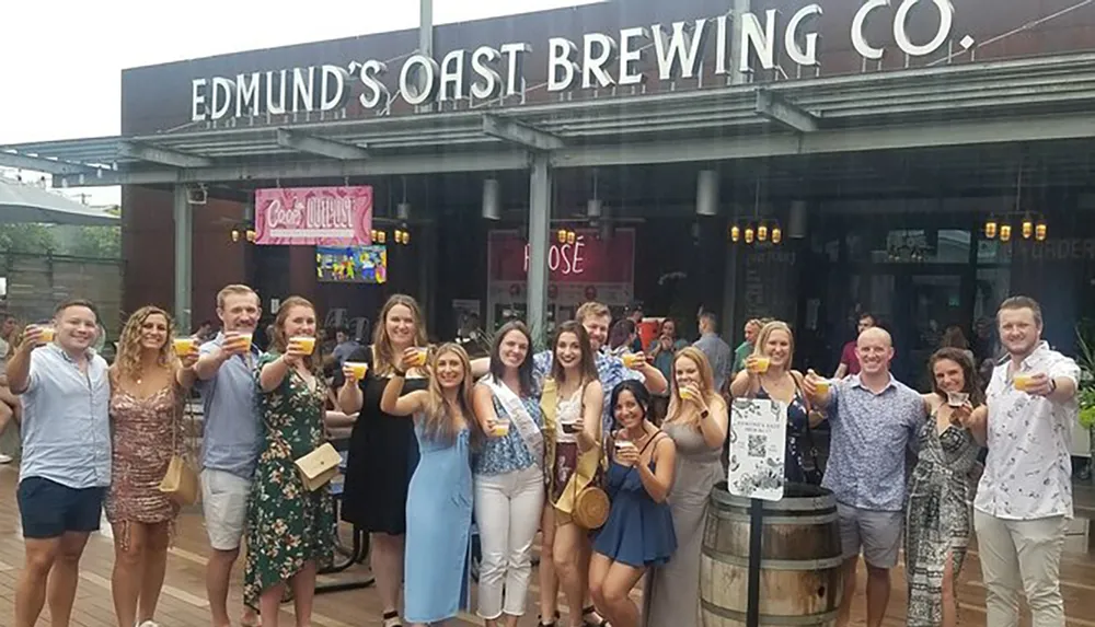 A group of cheerful people is toasting with drinks in front of the Edmunds Oast Brewing Co