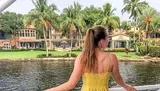 A person is looking towards a waterfront property lined with palm trees from a boat.