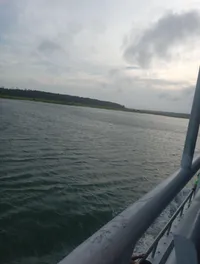 The image shows a tranquil body of water viewed from the railing of a boat with overcast skies and a glimpse of greenery at the distant shore.
