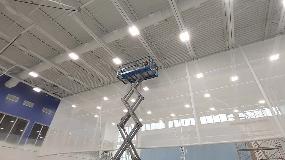 Workers inspection joist on lift in gymnasium