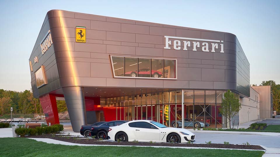 Two-story Ferrari car dealership exterior with exotic cars in showroom and in parking lot