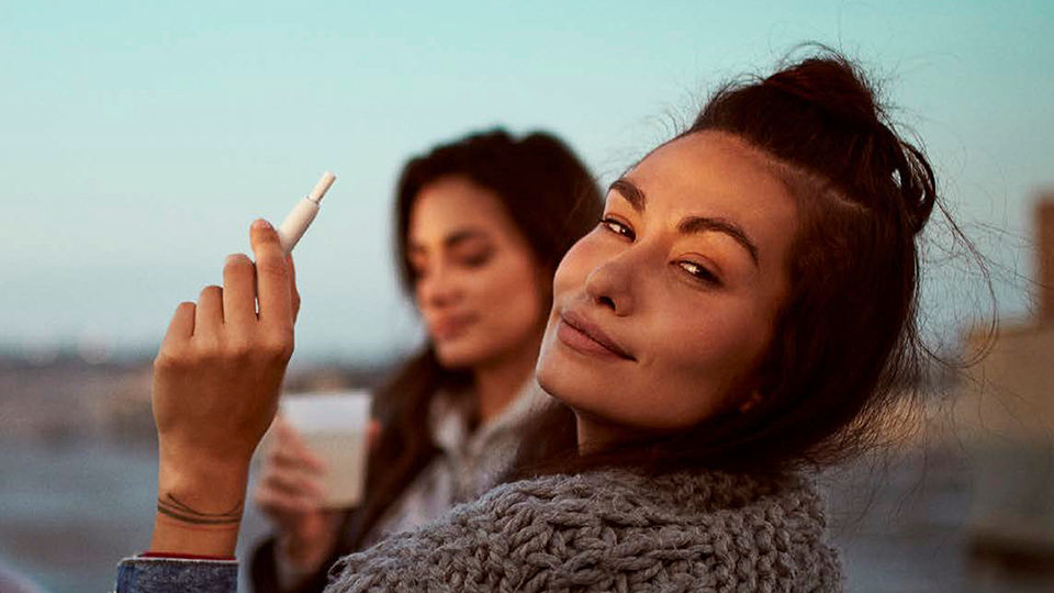 Two people with long brown hair, one of which is holding a vape pen