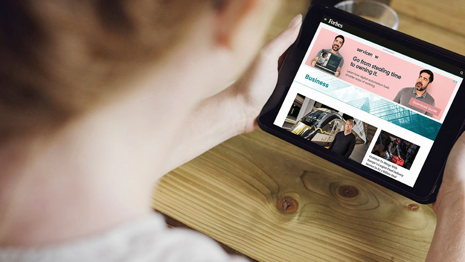 A person using a tablet device, looking at a Forbes article with ServiceNow included on it