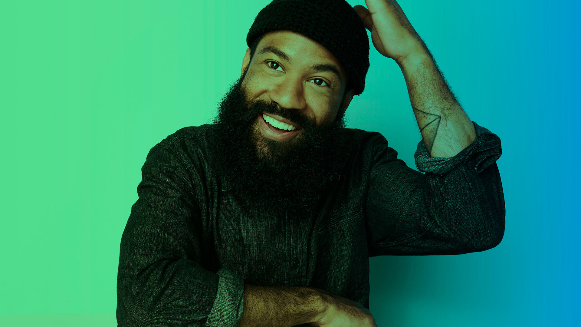 A happy and fashionable person, with a long beard, wearing a dark denim button up shirt