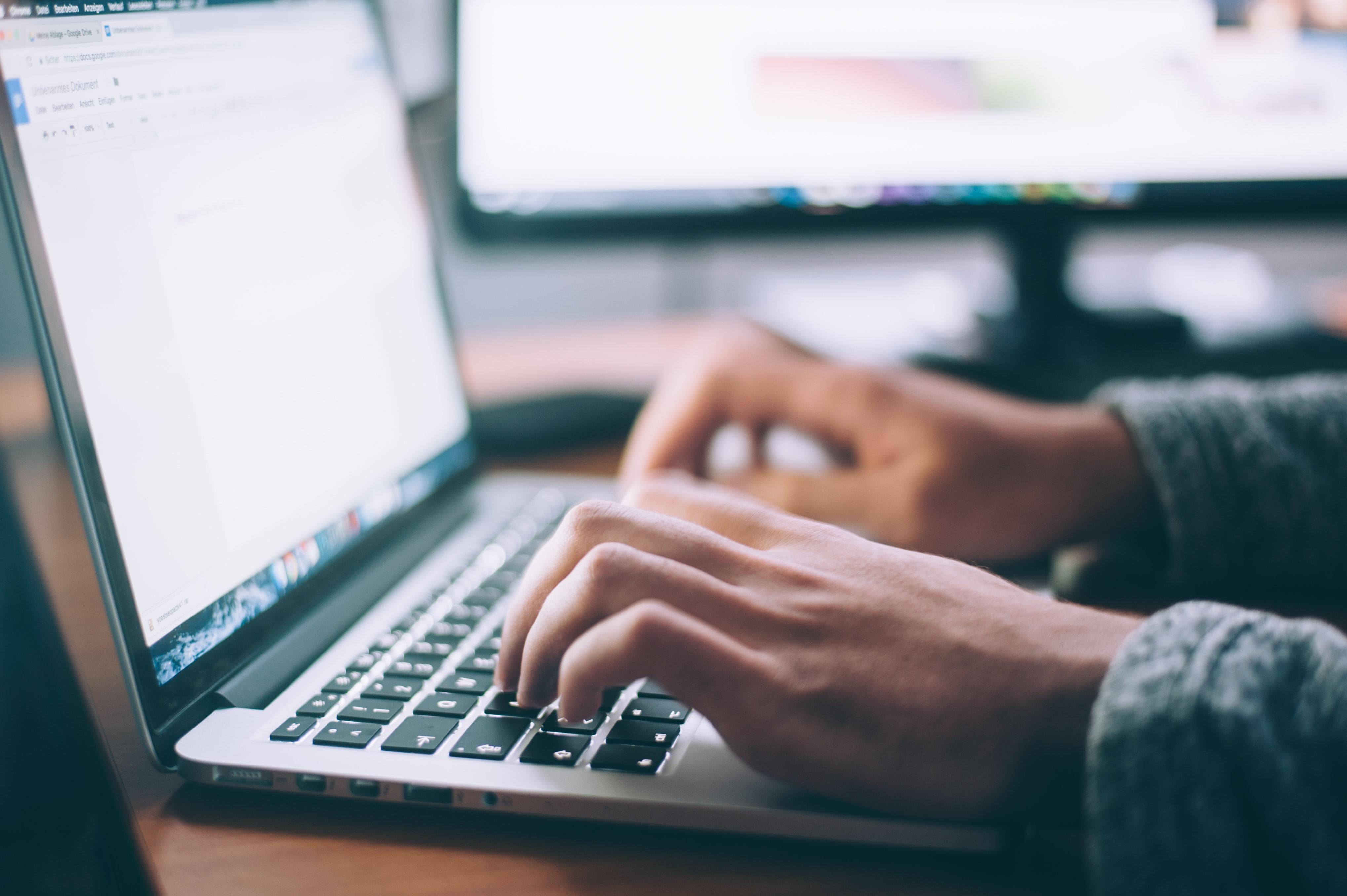 side view of a person's hands as they type on a laptop computer