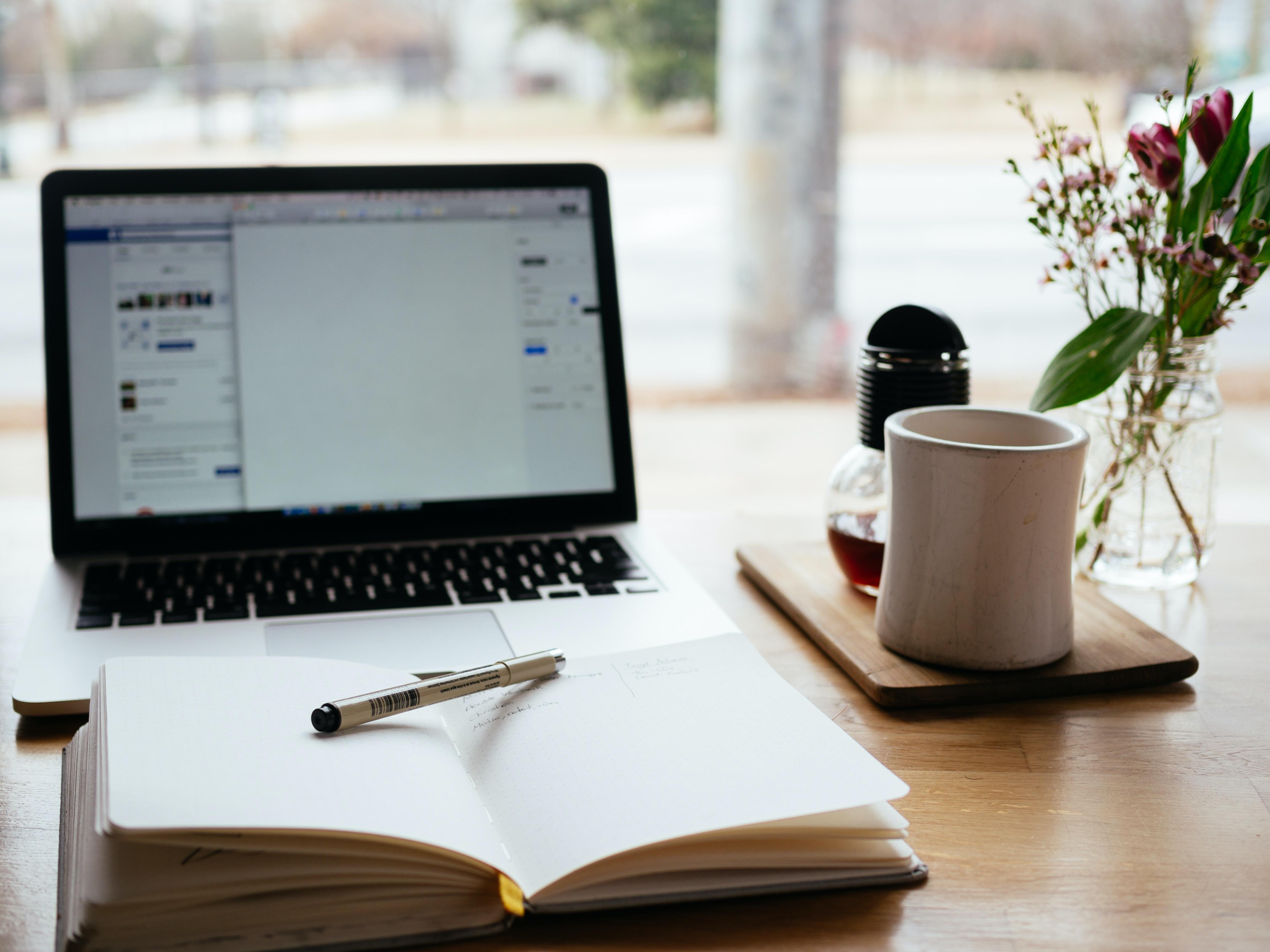 office table with laptop computer, open journal, and a vase of flowers