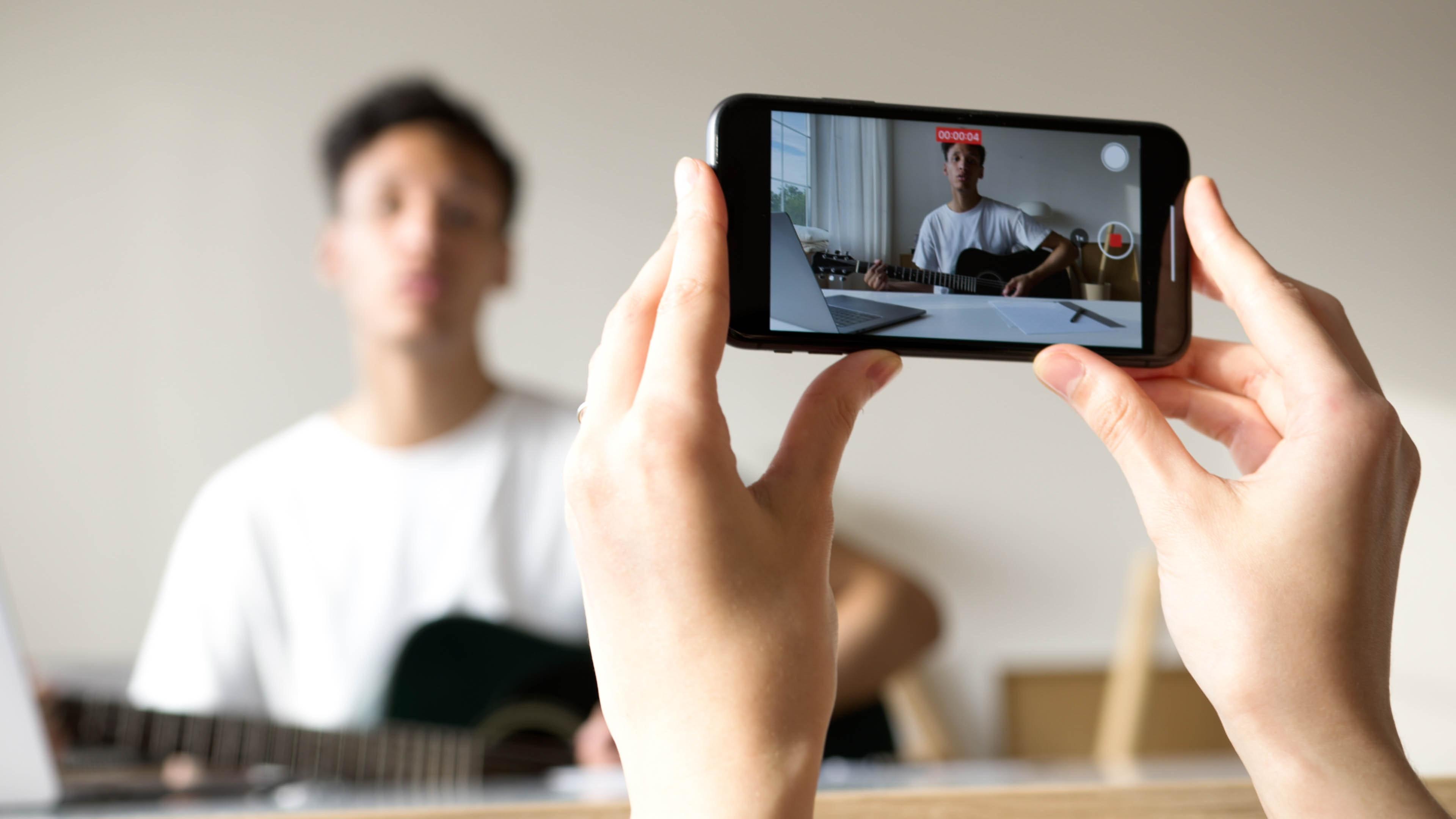 person holding up a mobile phone and filming a young man