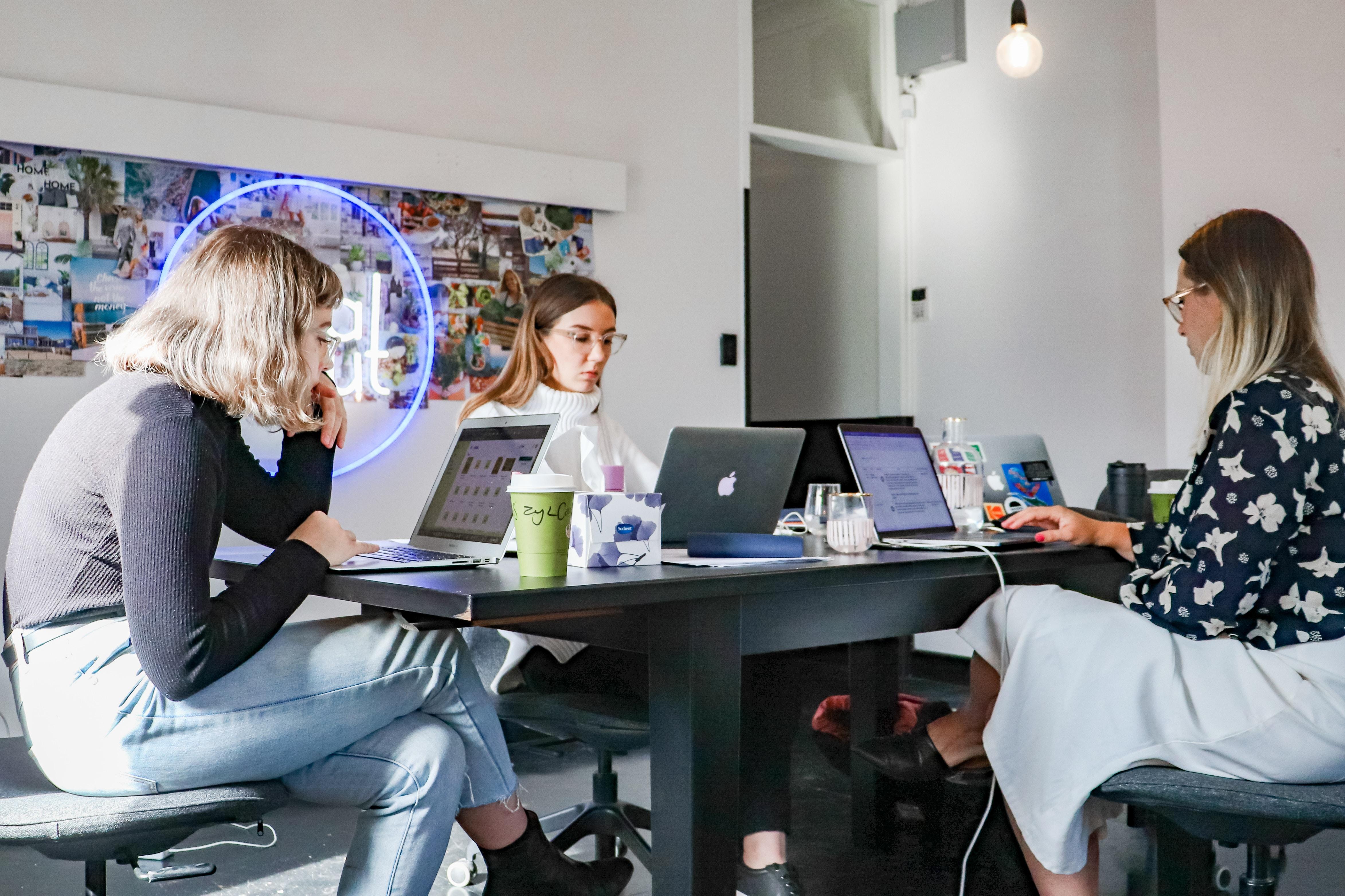 three women sitting around a table with laptop computers