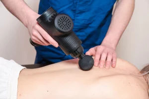Massage Gun Benefits: What You Need To Know Masseur massages a girl with a p