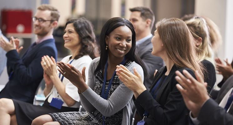 image of an audience clapping their hands focused on 2 women looking at each other and smiling