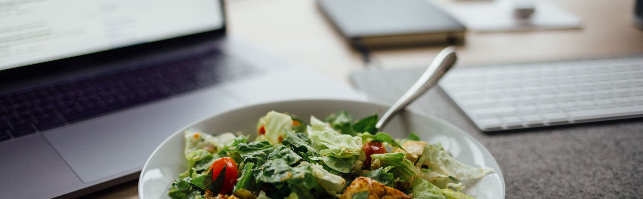 image of salad in white ceramic bowl with fork front of a laptop