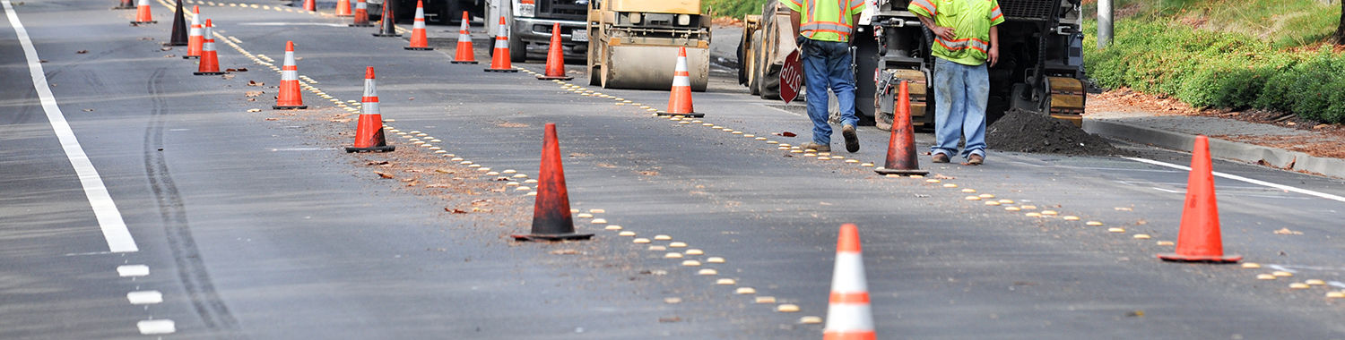 image show road work crew walking on the side of a road with their machines behind them and traffic cones in the road