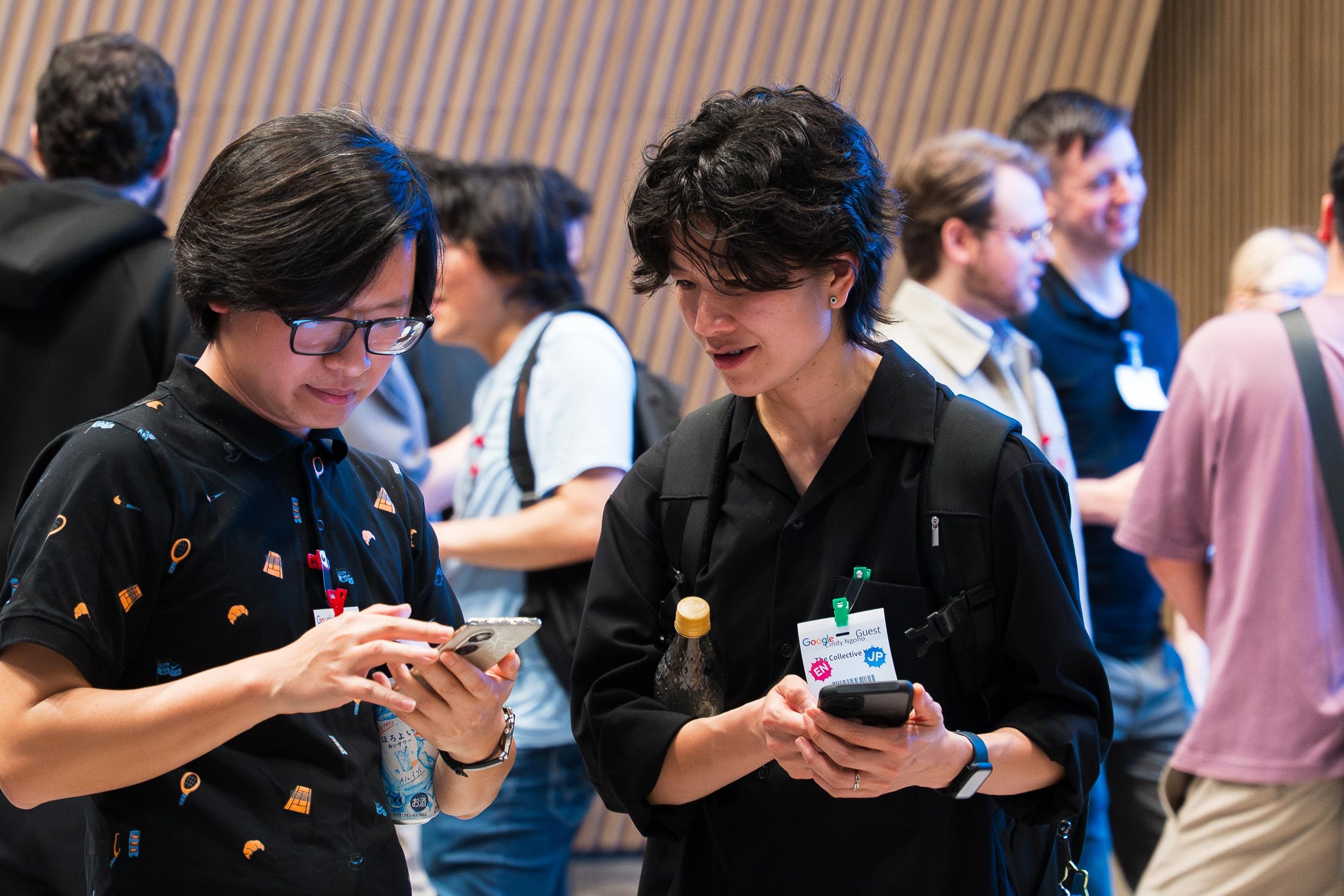 2名の参加者が経った状態でスマホを手に情報を交換している様子。背景にはほかの参加者が談笑している様子