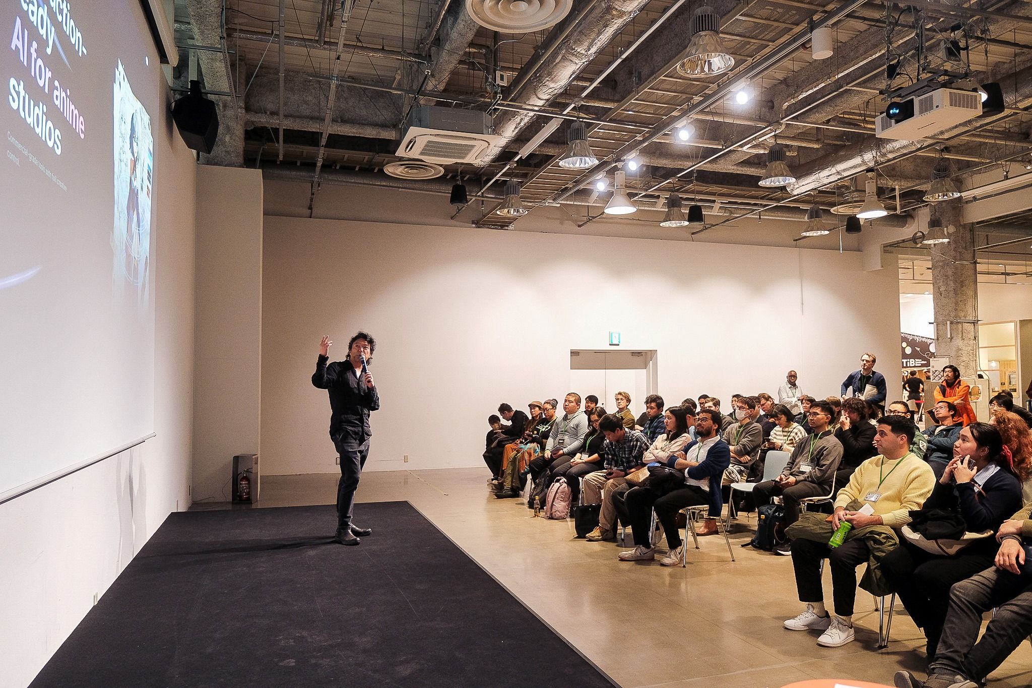 Tokyo Tech Jobs Nightの会場で、登壇者がステージに立ち、聴衆に向けてプレゼンテーションを行っている様子。A speaker presenting on stage at Tokyo Tech Jobs Night, speaking to a seated audience in a large event space.