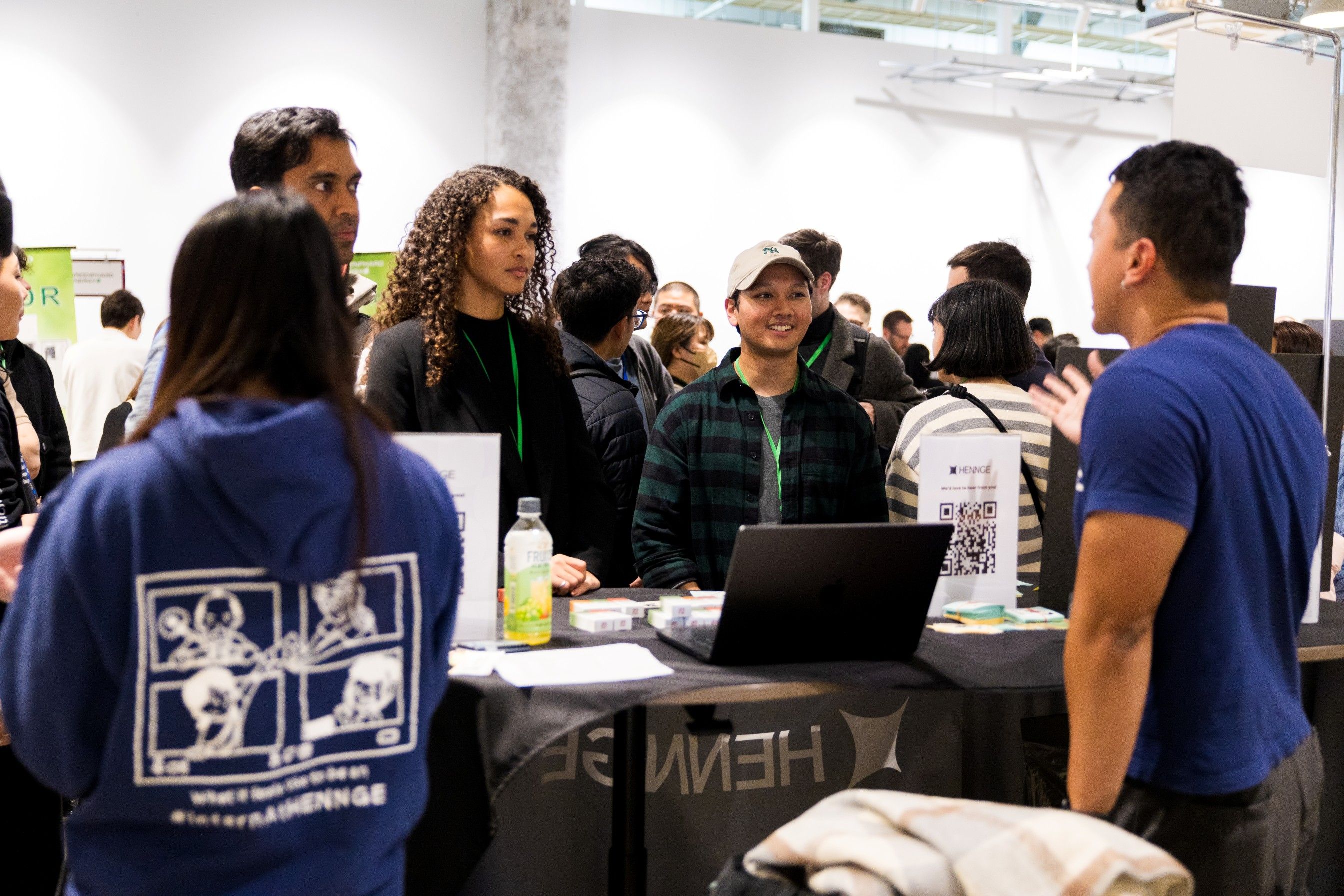 採用ブースで、参加者が企業担当者とノートパソコンや資料を囲んで会話している様子。Attendees talking with company representatives at a recruitment booth, with a laptop and informational materials on the table.