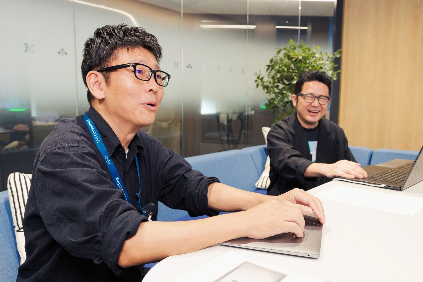 パソコンを前に話す荒木さんと、その後方で笑顔の岸本さん