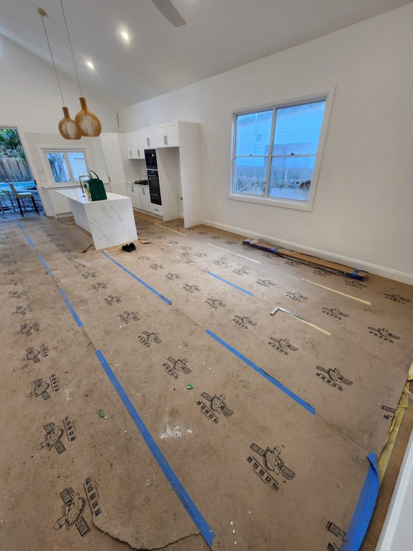 Open-plan kitchen with white cabinets and protected flooring during works