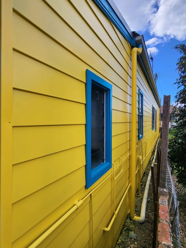 Yellow weatherboard wall with blue-framed windows after an exterior repaint
