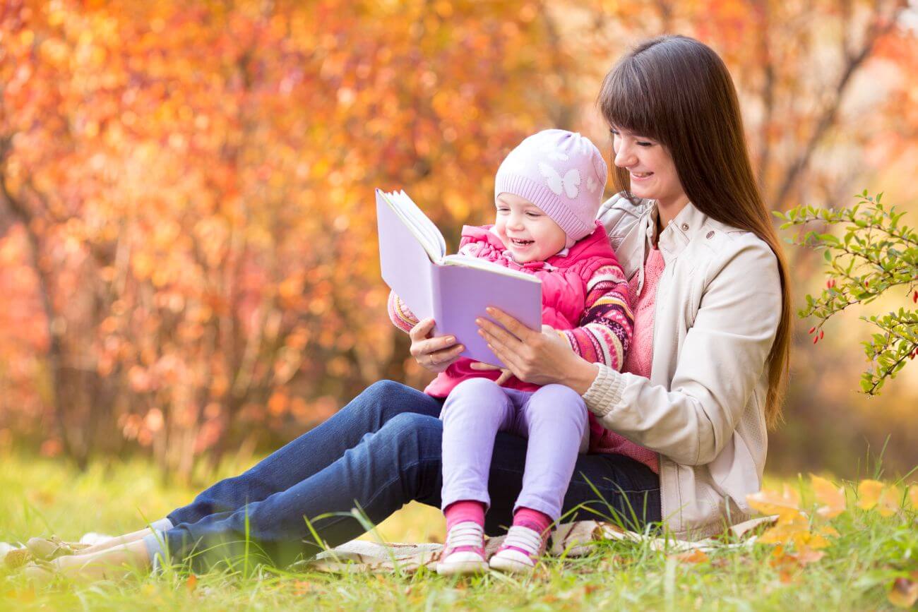mamka číta knihu svojej dcérke v parku na tráve