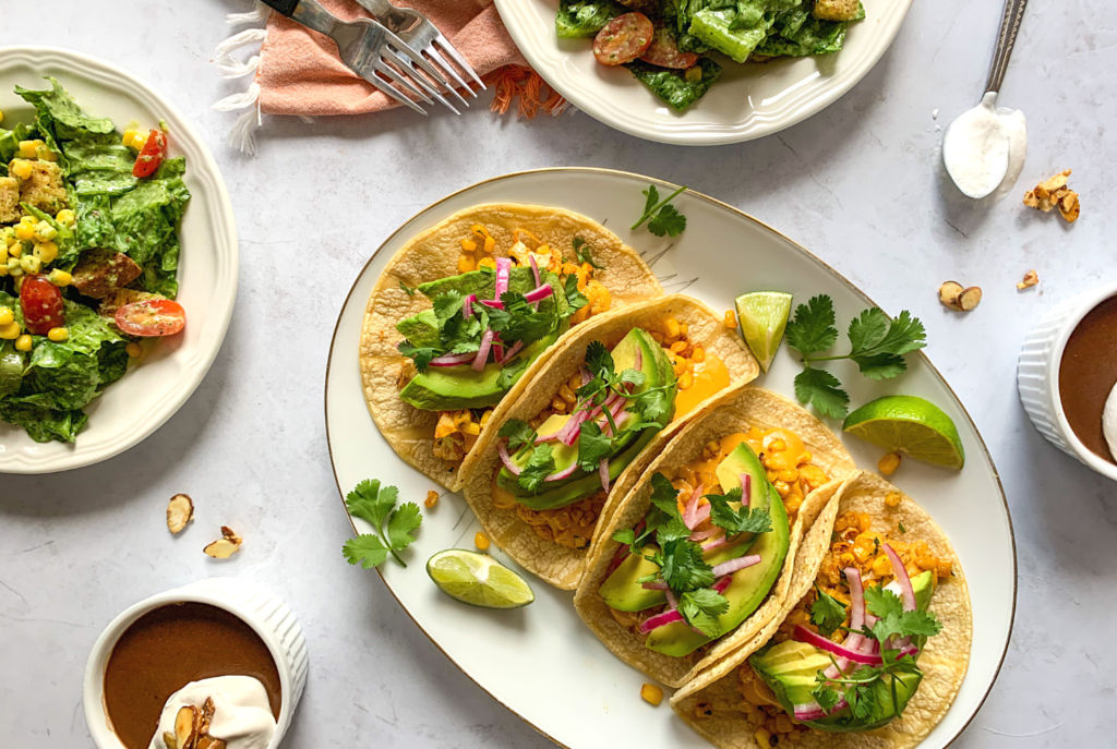 This image shows a platter of tacos, Mexican Caesar salad, and Mexican chocolate pots de creme.