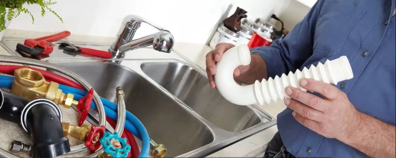 Close-up of a hand in a glove cleaning a foam-covered gold drain in a sink.