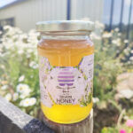 A jar of Devon Clear Honey from Quince Honey Farm against a floral background