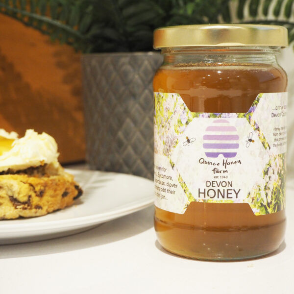 A 340g jar of Devon Clear Honey from Quince Honey Farm alongside a plate with a scone on