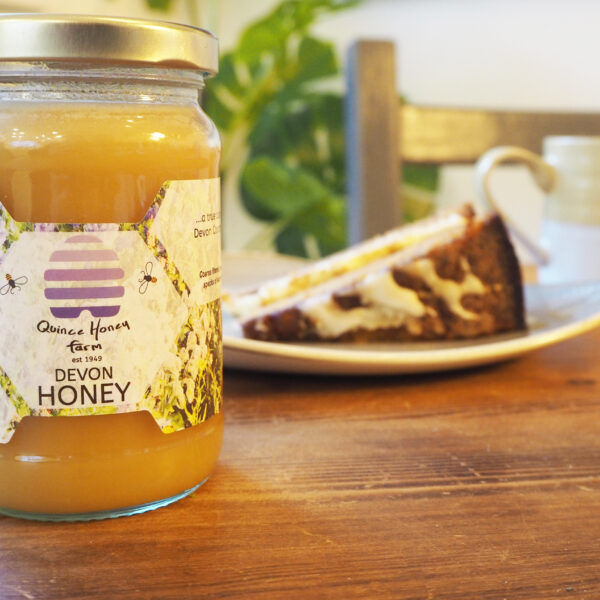 A jar of Devon Set Honey from Quince Honey Farm with a slice of cake in the background