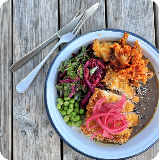 Image of a plate of food including chicken, edamame beans, cabbage, and pickled onion with a knife a fork