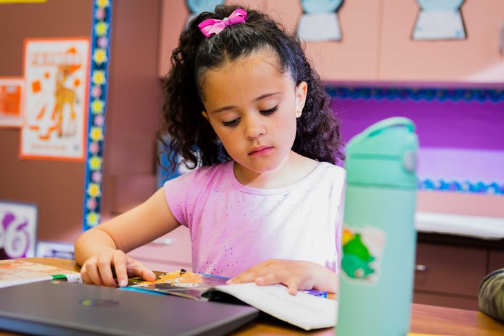 A young girl is sitting at her desk reading a book.