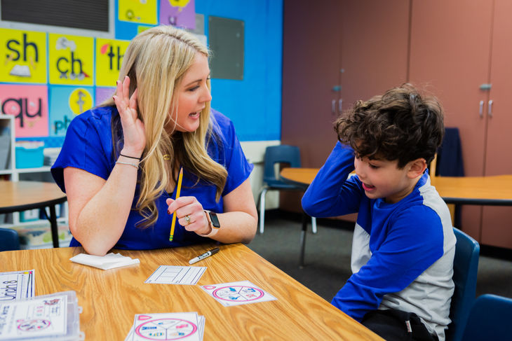 Teacher holds hand to ear while helping student learn to read closed syllable words