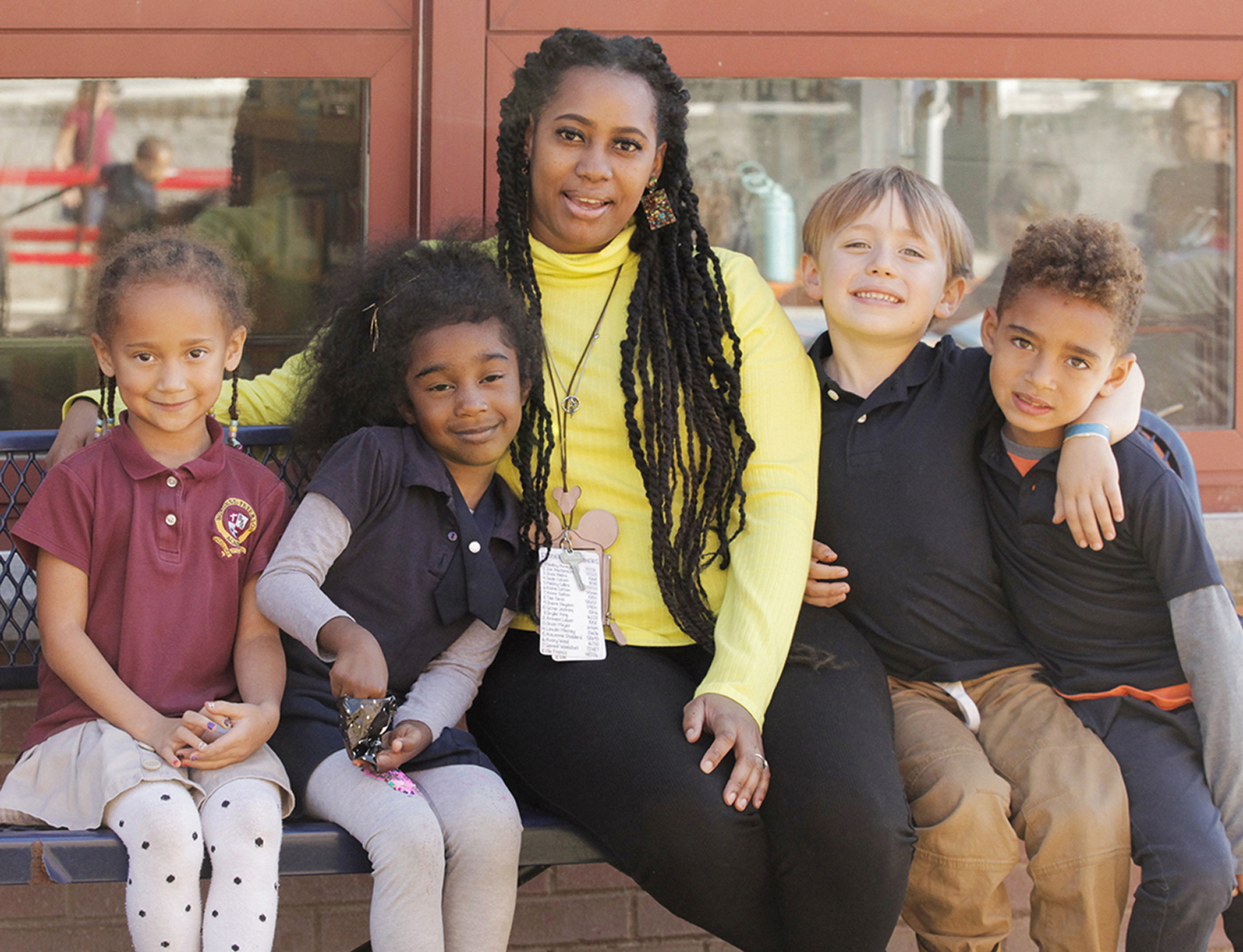 Teacher sitting outside on a bench with smiling students