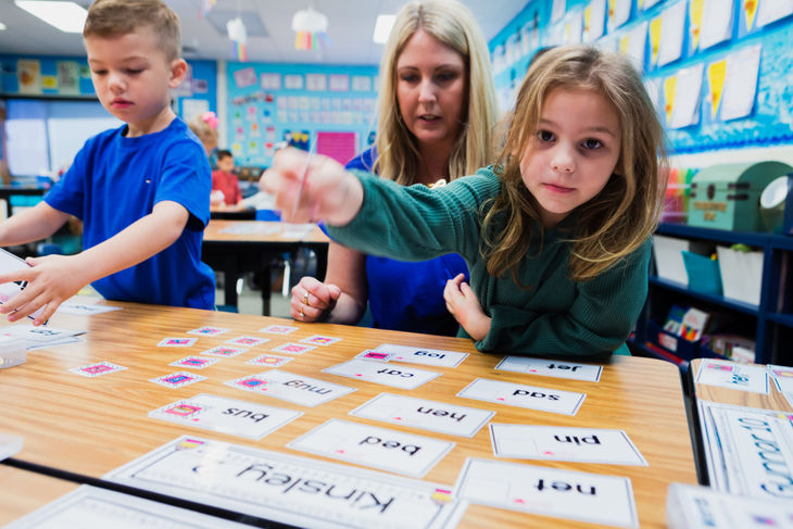 Teacher supports students during small group phonics instruction using word cards