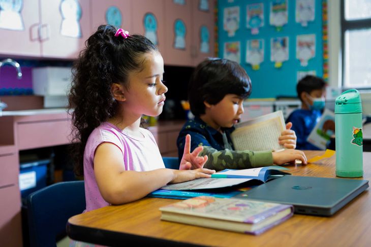 Hispanic girl reads a book in class