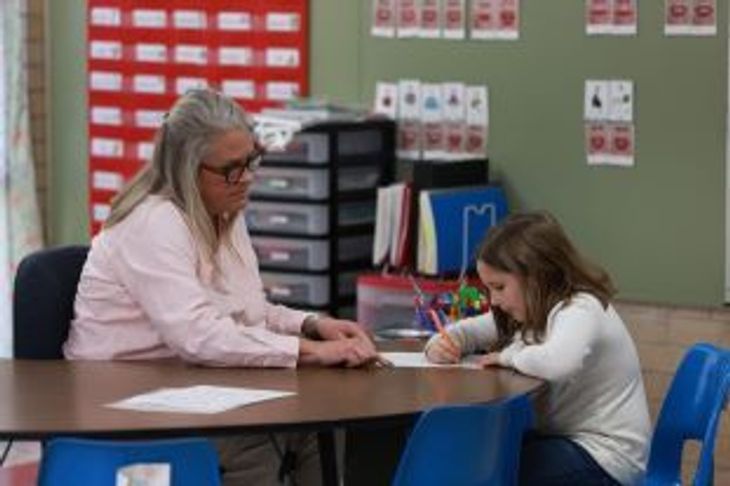 Teacher watching first grader write during assessment