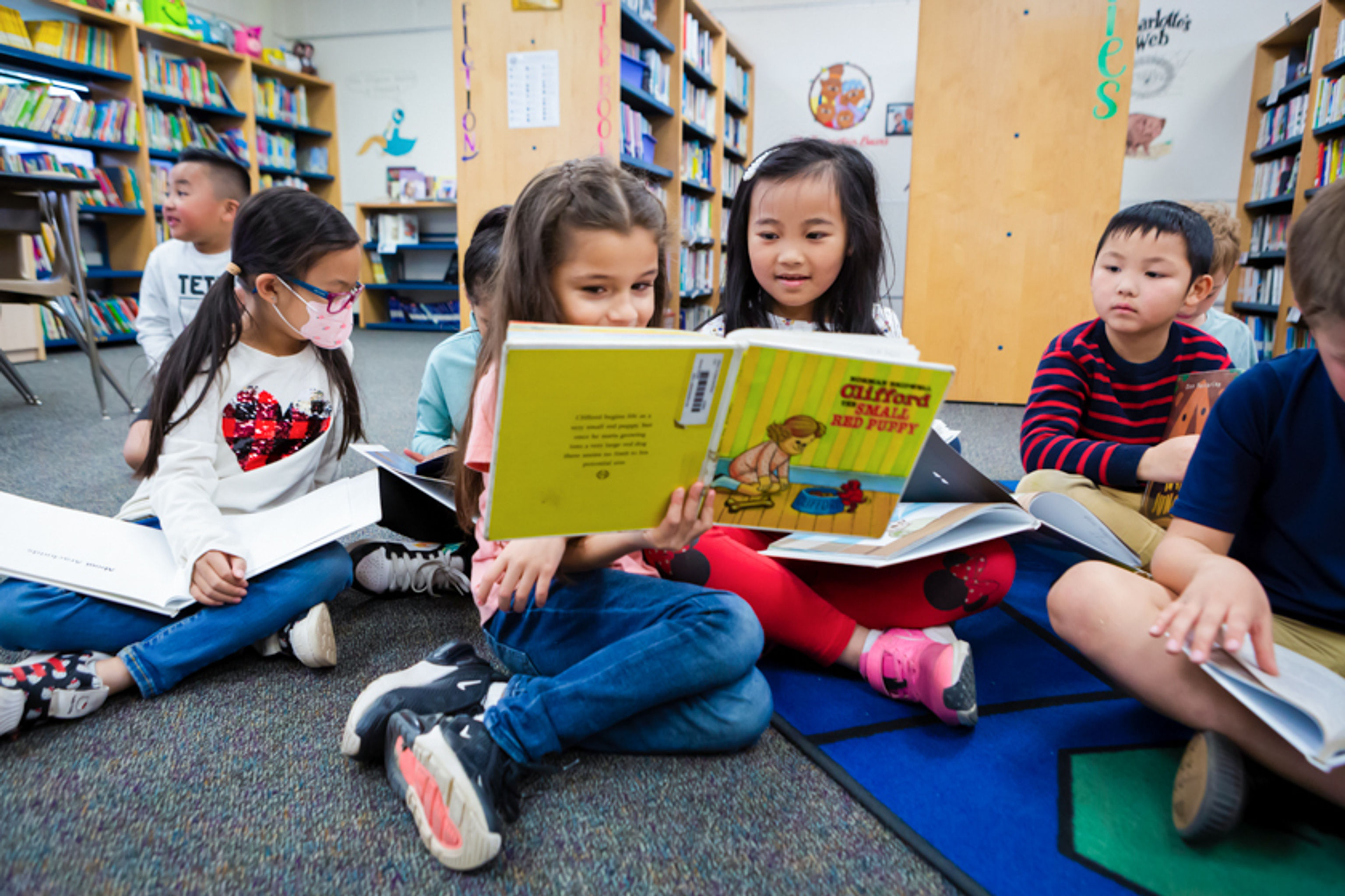 Two girls reading a book together while sitting in the library