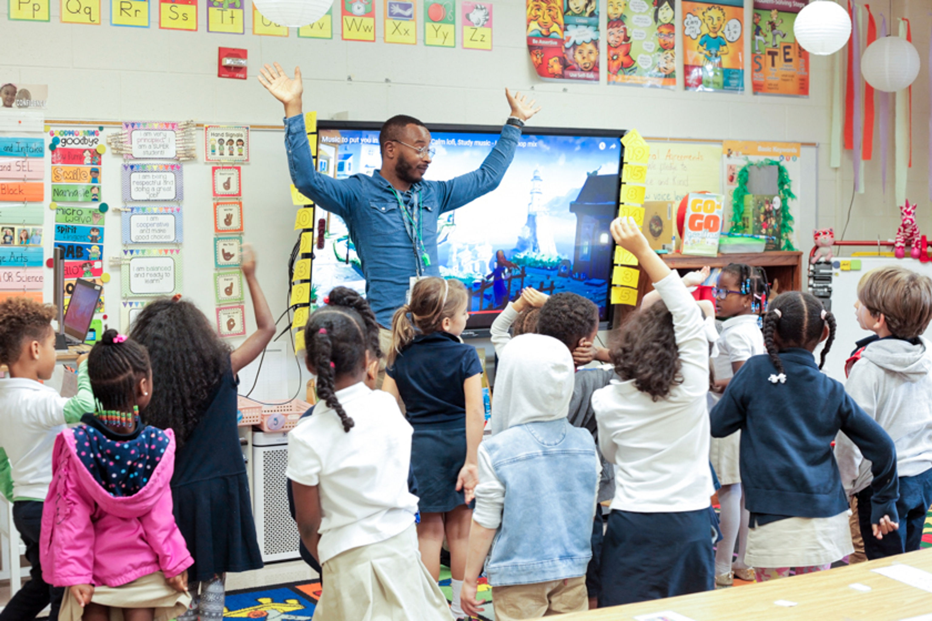 Excited teacher with raised hands in front of a group kindergarteners