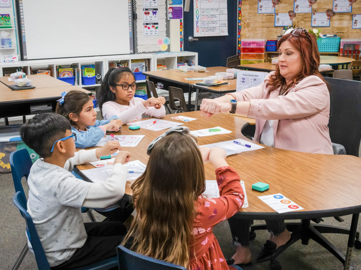 Teacher blends syllables with students using fisted hands