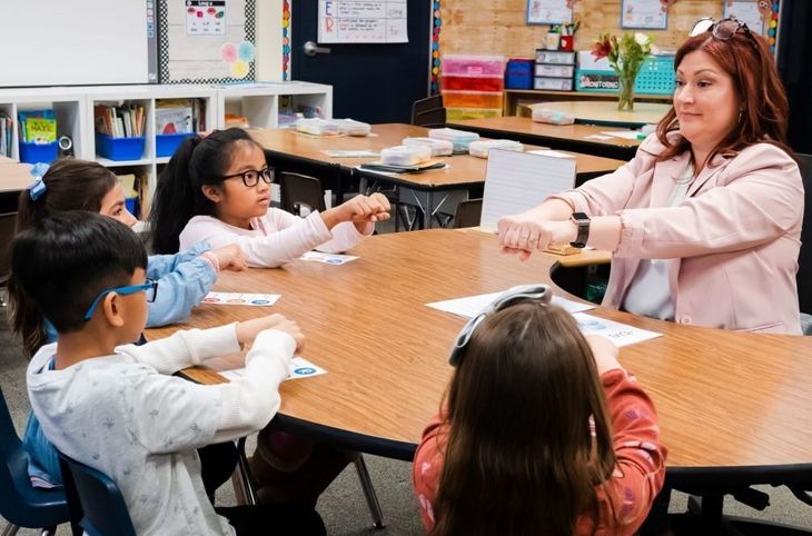 A first grade teacher models how to count syllables with a small group of students.