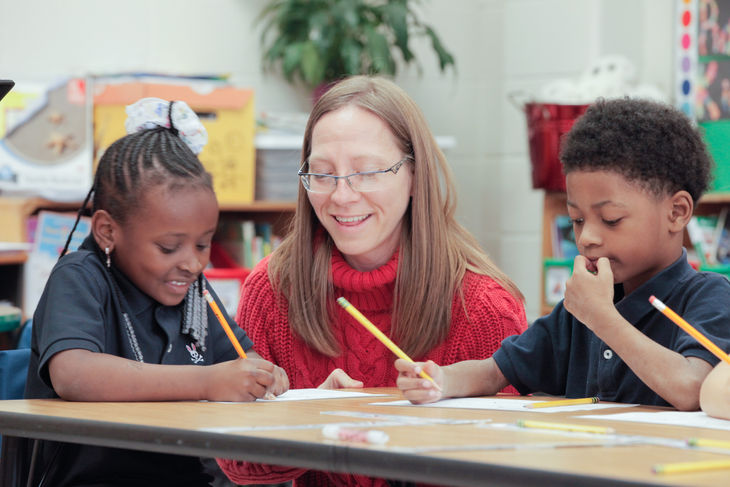 A teacher guides students with letter formation