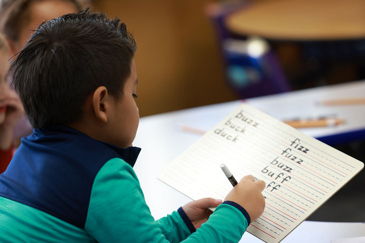 Child writing FLoSS(Z) words in a lined notebook