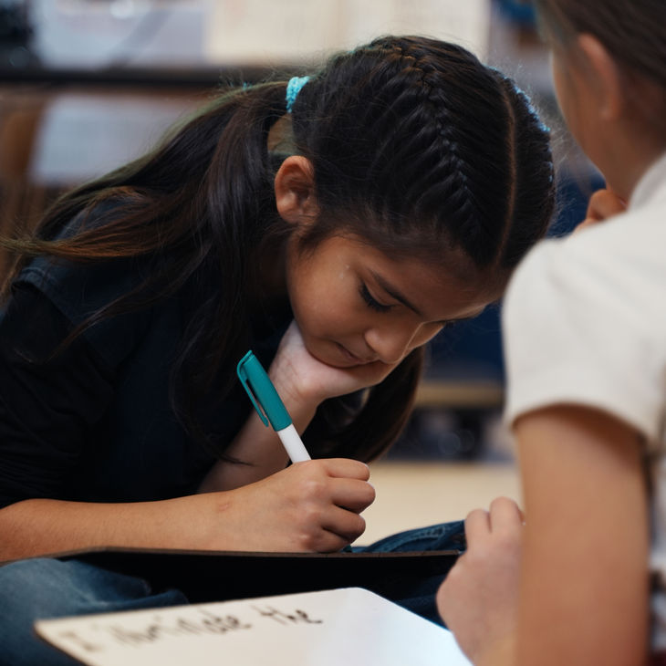 A girl writing on a wipe board in class